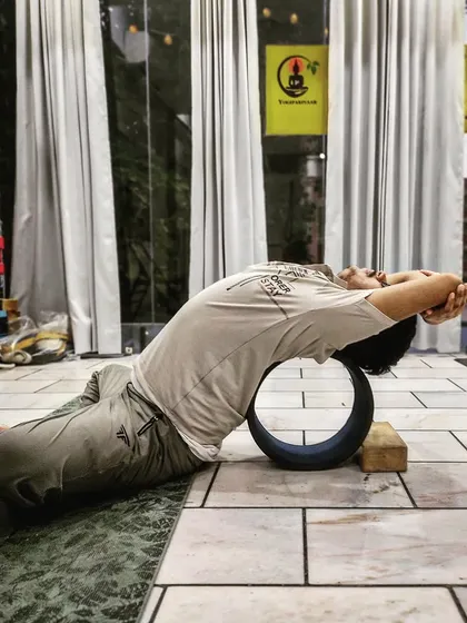 Using a yoga wheel for support in Supta Virasana (Reclining Hero Pose). This prop helps safely deepen the backbend, stretching the abdomen and relieving anxiety, making it a powerful tool in our therapeutic classes.