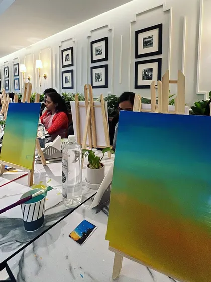 A view of the workshop table, showing two easels with gradient sky paintings in progress.