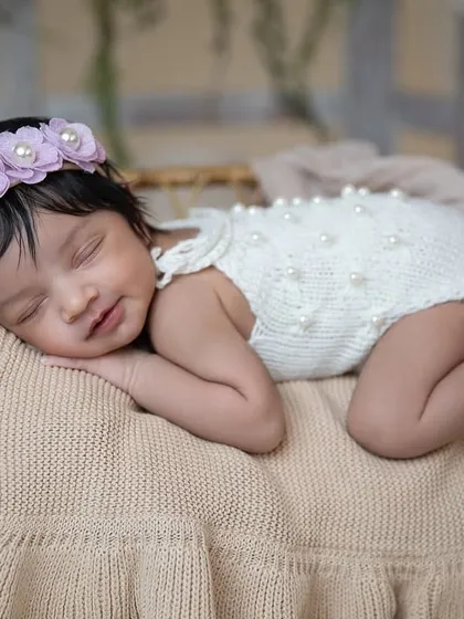 A sweet smile from a sleeping newborn is pure magic. This little girl, with a delicate floral headband, is dreaming peacefully during her studio session.