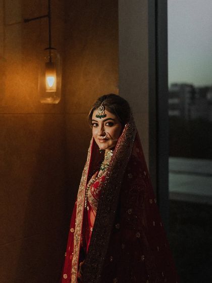 A moody and atmospheric portrait of the bride by a window. The warm indoor light contrasts with the evening sky, creating a cinematic and intimate feel.