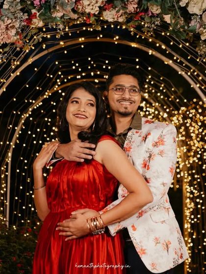 A couple poses under a beautifully decorated arch of flowers and fairy lights at night, creating a magical and romantic atmosphere.