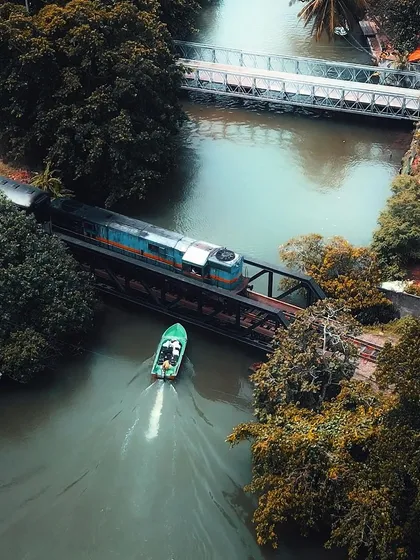 A perfectly timed aerial shot of a train and a boat crossing paths in Thailand, showcasing the beautiful intersection of different modes of transport.