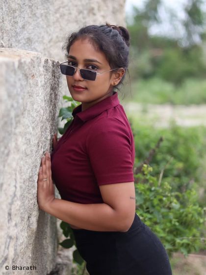 A confident portrait against a large rock, using sunglasses as a prop to add style and attitude.
