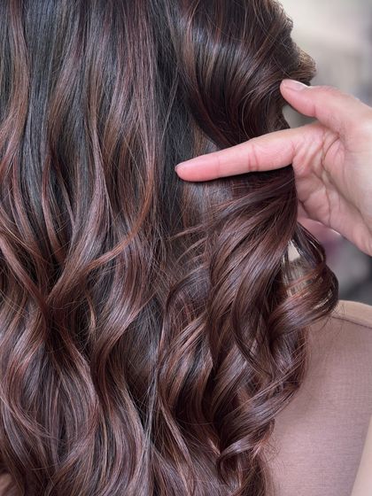 A close-up showing a stylist's hand defining a perfect chocolate-toned curl, emphasizing the texture and shine.