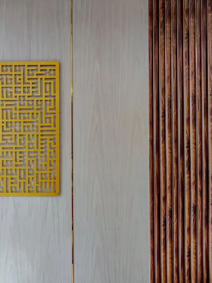 A detail shot of a wall treatment, combining light wood veneer, fluted dark wood panels, and a decorative golden jaali screen. This mix of modern and traditional elements is a signature of our style.