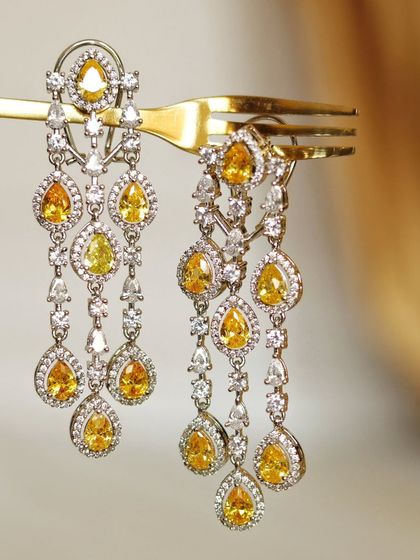Sometimes the simplest prop makes the boldest statement. A single golden fork holds these sunshine-yellow chandelier earrings, creating an unexpected and elegant composition that highlights their sparkle.