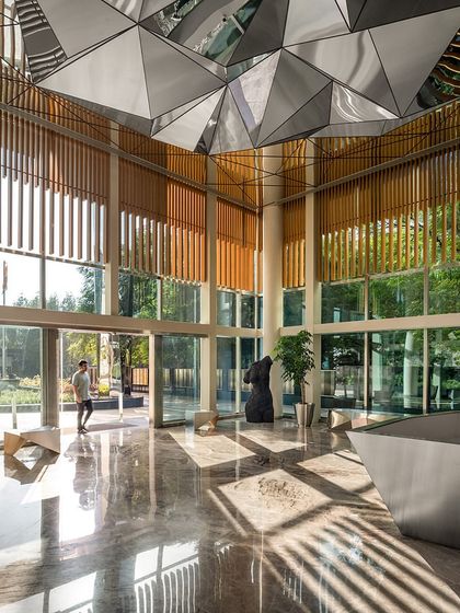 Sunlight streams into the double-height directors' reception area, highlighting the polished marble floors and the interplay between the wooden wall paneling and the reflective steel ceiling element.