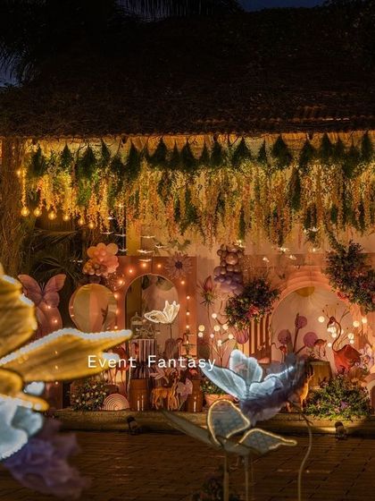 A magical night view of Hitanshi's enchanted garden. The entire setup is illuminated with warm lights, with glowing butterfly props in the foreground, creating a truly breathtaking fantasy world.