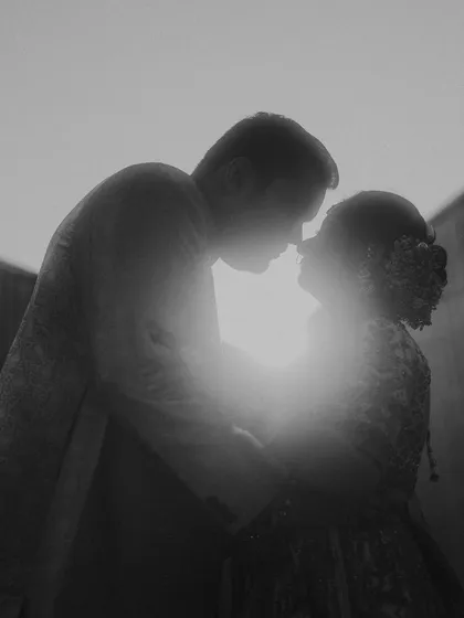 A powerful black and white silhouette of a couple about to kiss, backlit by the sun. This artistic engagement photo plays with highlights and shadows to create a timeless, dramatic, and emotional portrait.