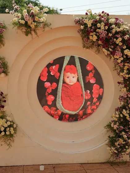 A creative backdrop for a cradle ceremony, featuring a large custom portrait of the baby. The wall is adorned with floral arrangements, making the baby the star of the decor.