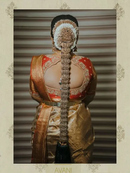 A full back view of a bride's muhurtham look. The red blouse features a beautiful cutout design, complemented by the traditional South Indian jada hairstyle with temple jewelry.