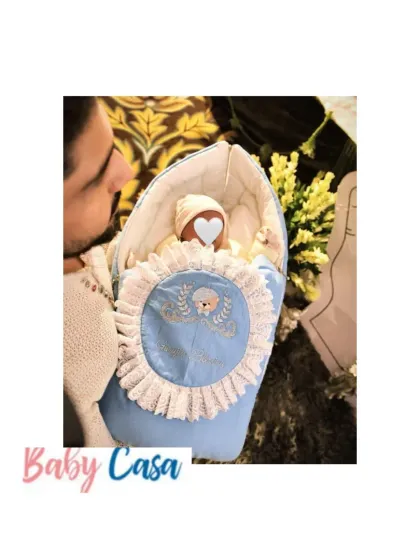 A proud father holds his baby, who is nestled in a personalized blue sleeping bag. It’s a joy to see my creations being part of these first family moments.