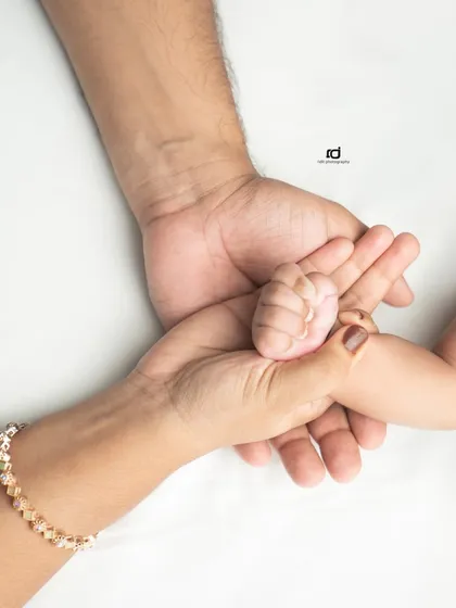 Three hands joined as one. A mother's and father's hands gently hold their baby's tiny fist, representing the creation of their new family unit.