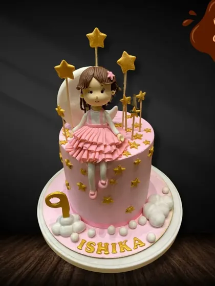 A lovely pink cake for a ninth birthday, featuring a doll with angel wings. The cake is adorned with golden stars, creating a dreamy, celestial theme for a little star.