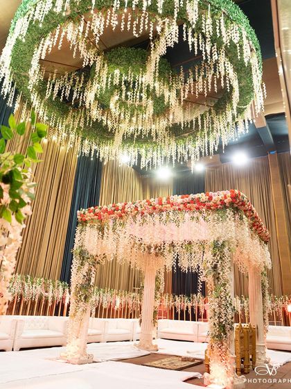 A stunning wide shot of a floral mandap, beautifully decorated with white and red flowers, ready for the wedding ceremony. We capture the grandeur of your decor.