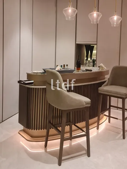 This artfully designed bar area captures attention with its fluted panels and gracefully curved form. Paired with elegant, high-backed chairs, the sleek design invites one to enjoy leisurely sips in a stylish and sophisticated setting.