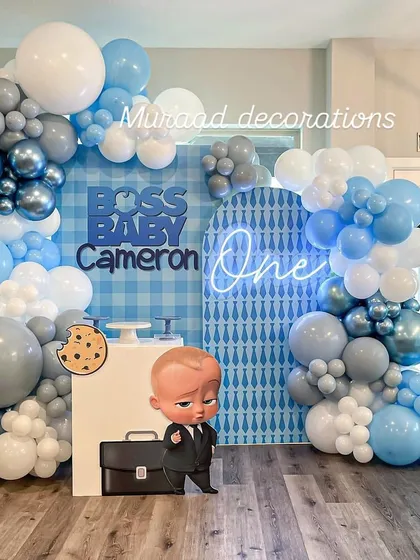 A clean and modern Boss Baby setup for a first birthday. We used a blue and white checkered backdrop, a neon 'One' sign, and an organic balloon garland in shades of blue, grey, and white.