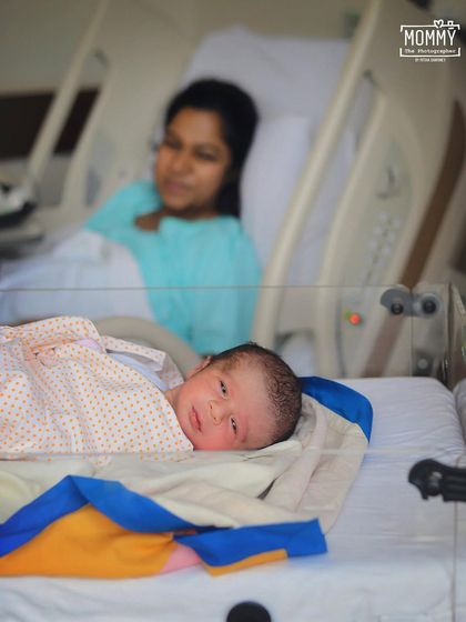 This photo captures the reality of the hospital room, with the new mother resting in bed while her baby lies in the foreground. It’s a quiet, authentic moment from the first few days.