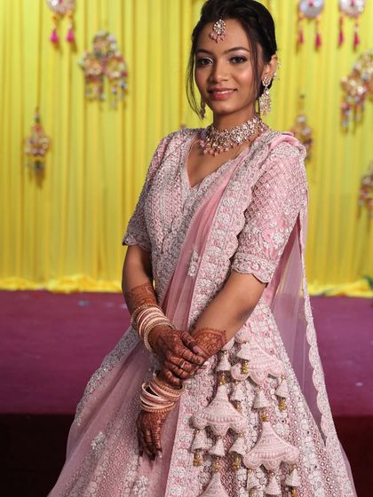 A close-up of a bride in a soft pink lehenga, highlighting the delicate embroidery and the beautiful tassel work on the skirt.
