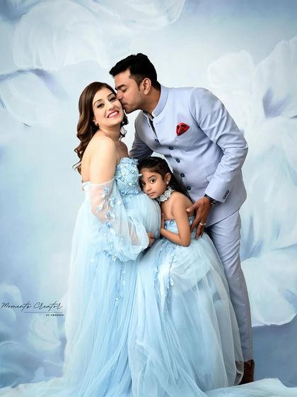 A loving family embrace during their maternity session. The father-to-be kisses his wife's forehead as their daughter snuggles close, all in coordinated pastel blue against a dreamy floral background.