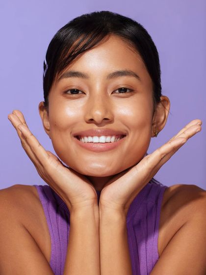 A clean beauty shot where the simple purple tank top complements the model's glowing skin and the product's color scheme.