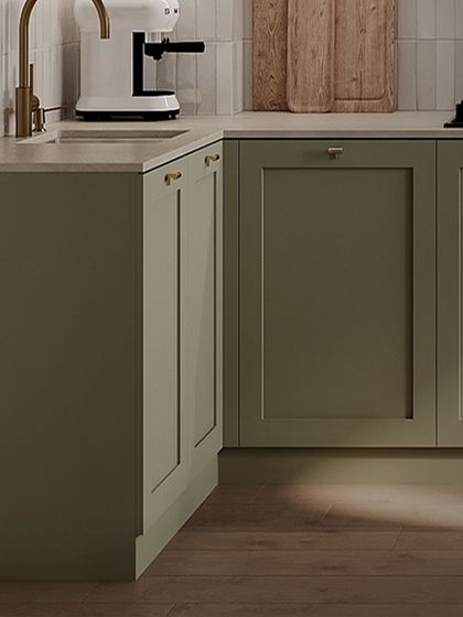 A closer look at the details of this green shaker kitchen. The simple brass knobs and warm wood flooring complement the cabinet color, while the white countertop keeps the space feeling bright.