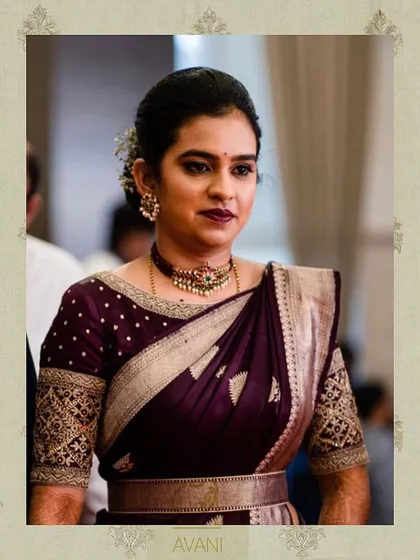 A client wearing a deep wine-colored blouse with elbow-length sleeves. The sleeves feature traditional gold embroidery, perfectly complementing her Kanchipuram silk saree.