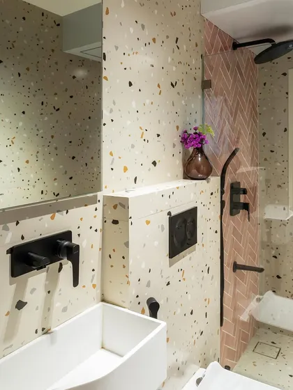 A bathroom that plays with pattern and texture. The terrazzo-style tiles are paired with pink herringbone tiles in the shower, creating a fun, contemporary look with matte black fixtures.