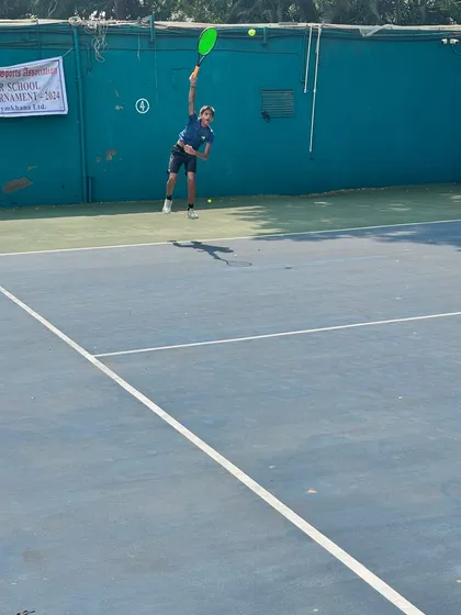 A player mid-serve, showcasing the power and technique we cultivate at our academy during the Inter School Tennis Tournament.