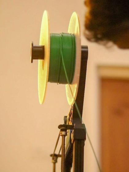 A spool of green PLA filament is ready to be fed into the printer. We use this biodegradable plastic to ensure our creations are as eco-friendly as possible.