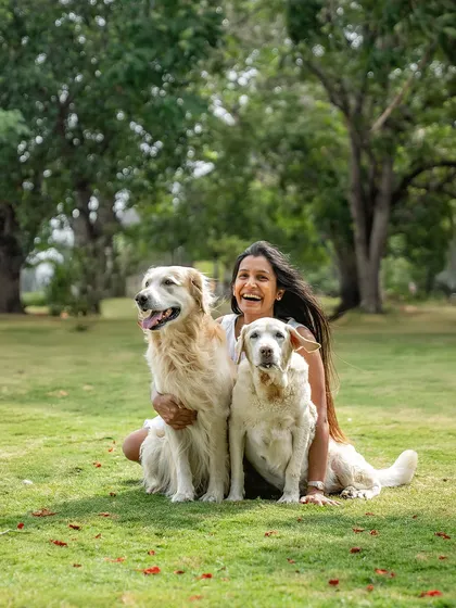 A woman and her daughter share a laugh with their two beautiful dogs, a Golden Retriever and a Labrador, during a sunny day at the park. This photo radiates pure joy and the happiness of spending time together as a family.