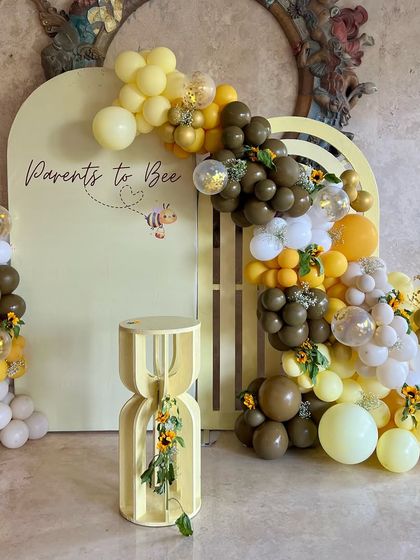 A full view of the 'Parents to Bee' baby shower decor. The setup features a honeycomb-inspired backdrop, a modern side table, and a beautiful balloon arch in shades of yellow, brown, and white.