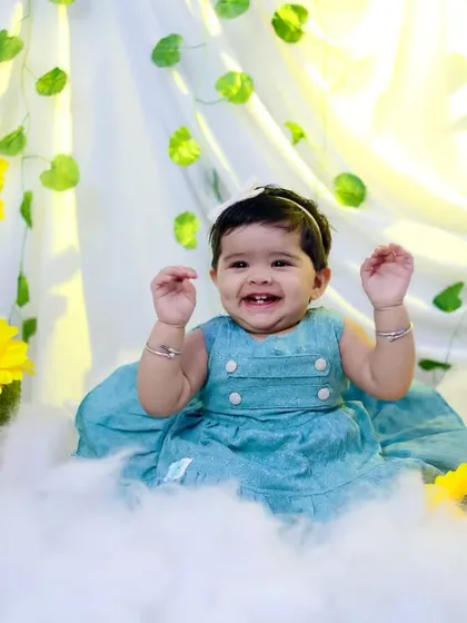 An expressive, happy portrait of a baby girl surrounded by sunflowers and clouds. Her big smile says it all.