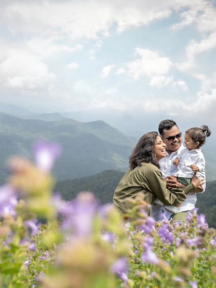 A breathtaking wide shot of the family on a mountaintop, with the Neelakurinji flowers in the foreground. This photo captures both the intimate family moment and the grand, beautiful landscape.