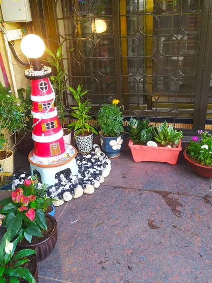 A cozy corner of a patio decorated with a variety of potted plants. We also help with decorative elements like this lighthouse lamp to complete the garden's theme.