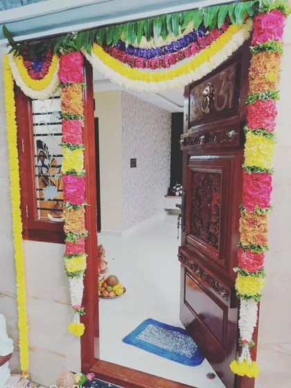 The main door decoration is key for any auspicious event. We use fresh, vibrant flowers to create these intricate garlands, framing the beautiful carved wood and setting a festive tone right from the entrance.
