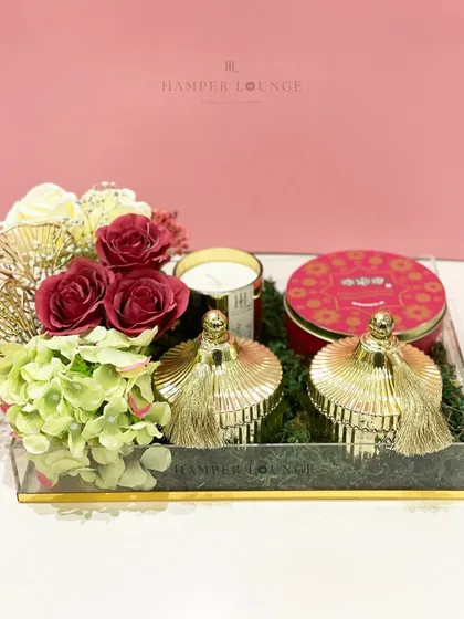This acrylic tray hamper for Eid is a feast for the eyes. It features golden tassel-topped jars, a scented candle, and a tin of festive sweets, all nestled on a bed of green moss and florals.