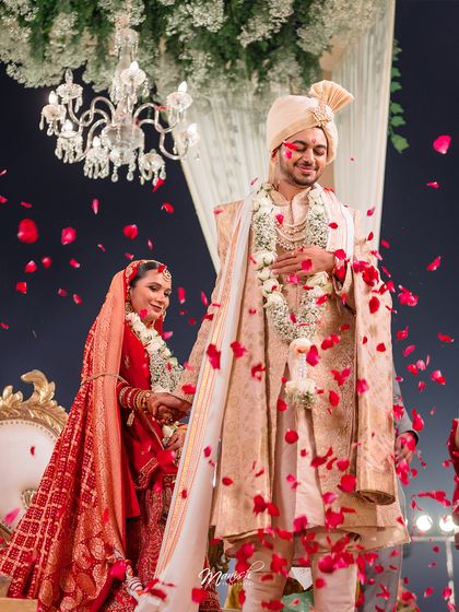 The newlyweds walk together, showered in red rose petals, a moment of pure celebration and romance.