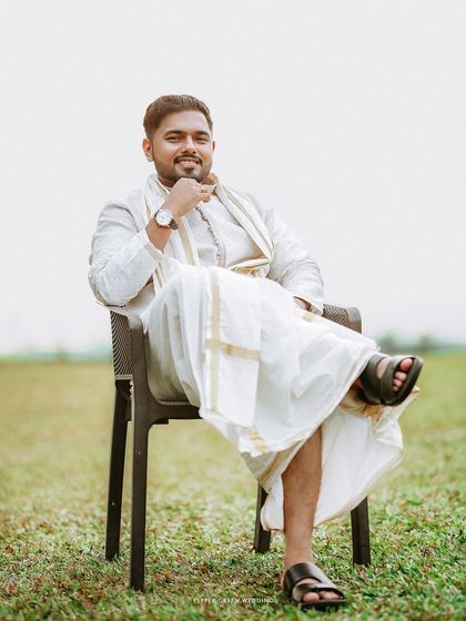 A handsome portrait of the groom in his traditional white and gold attire, seated casually and confidently.