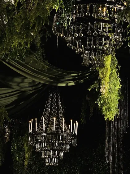 A close-up of the lighting and floral design for an enchanted forest theme. I suspended ornate black crystal chandeliers amidst lush, hanging greenery to create a dramatic contrast and a sense of mystery and elegance.