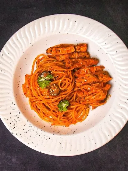 A full plate of red sauce spaghetti with grilled chicken, shot from above on a dark background. This provides a clear and stylish view of the entire dish.