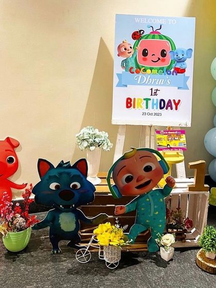 A welcome area for a Cocomelon themed party, with character standees and a personalized welcome sign on an easel.