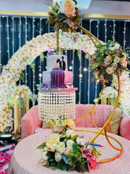 A beautiful cake table setup that also serves as a photo corner. The suspended cake stand is a unique touch, framed by a floral arch and a comfortable sofa for the couple.