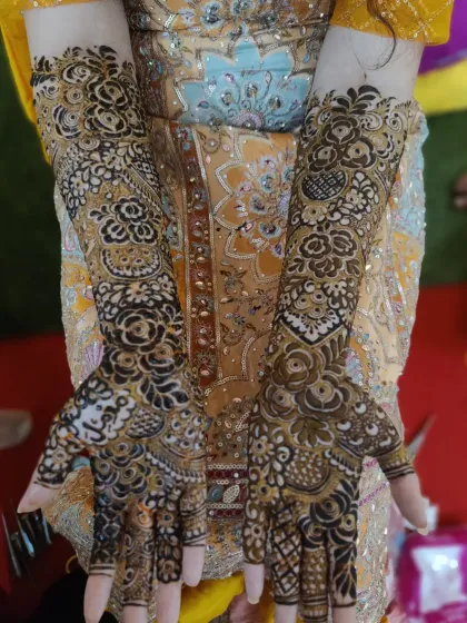 This bride's hands are adorned with a beautiful floral mehndi design that complements her yellow outfit perfectly. The pattern extends from her fingertips to her elbows.