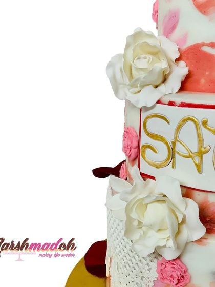Detail shot of the 3-tier cake, showing the handmade white fondant flowers and the elegant gold lettering of the name "Satviki".