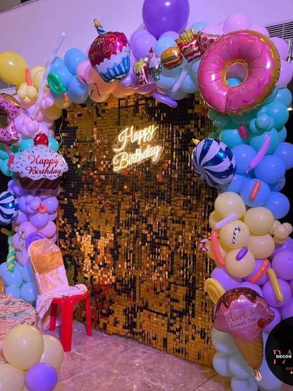 Another view of the candy-themed photo backdrop with a gold sequin wall and fun, colorful balloon sculptures.