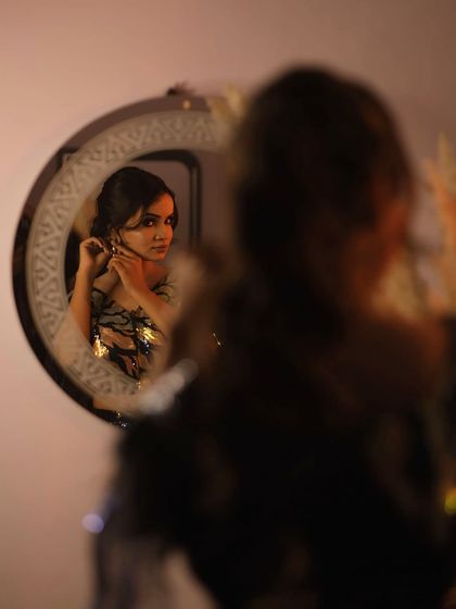 A behind-the-scenes style portrait, capturing the model adjusting her earring in the mirror, adding a candid and personal touch to the glamour shoot.