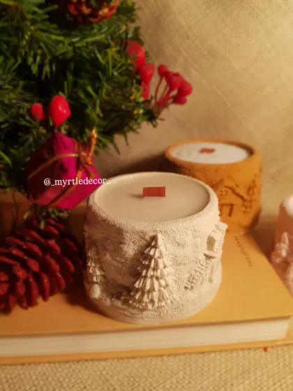 Our white Winter Lights Jar Candle styled on a book with festive greenery. It’s a perfect little piece to create a cozy reading nook during the holidays.