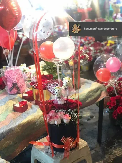This celebration box is designed for pure fun and affection. It combines pink and red roses with adorable teddy bears and a cascade of festive red and white balloons, making it a wonderful surprise gift.