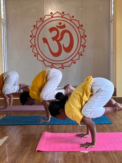 Students build upper body strength and balance by practicing Bakasana (Crow Pose) during a beginner level class.
